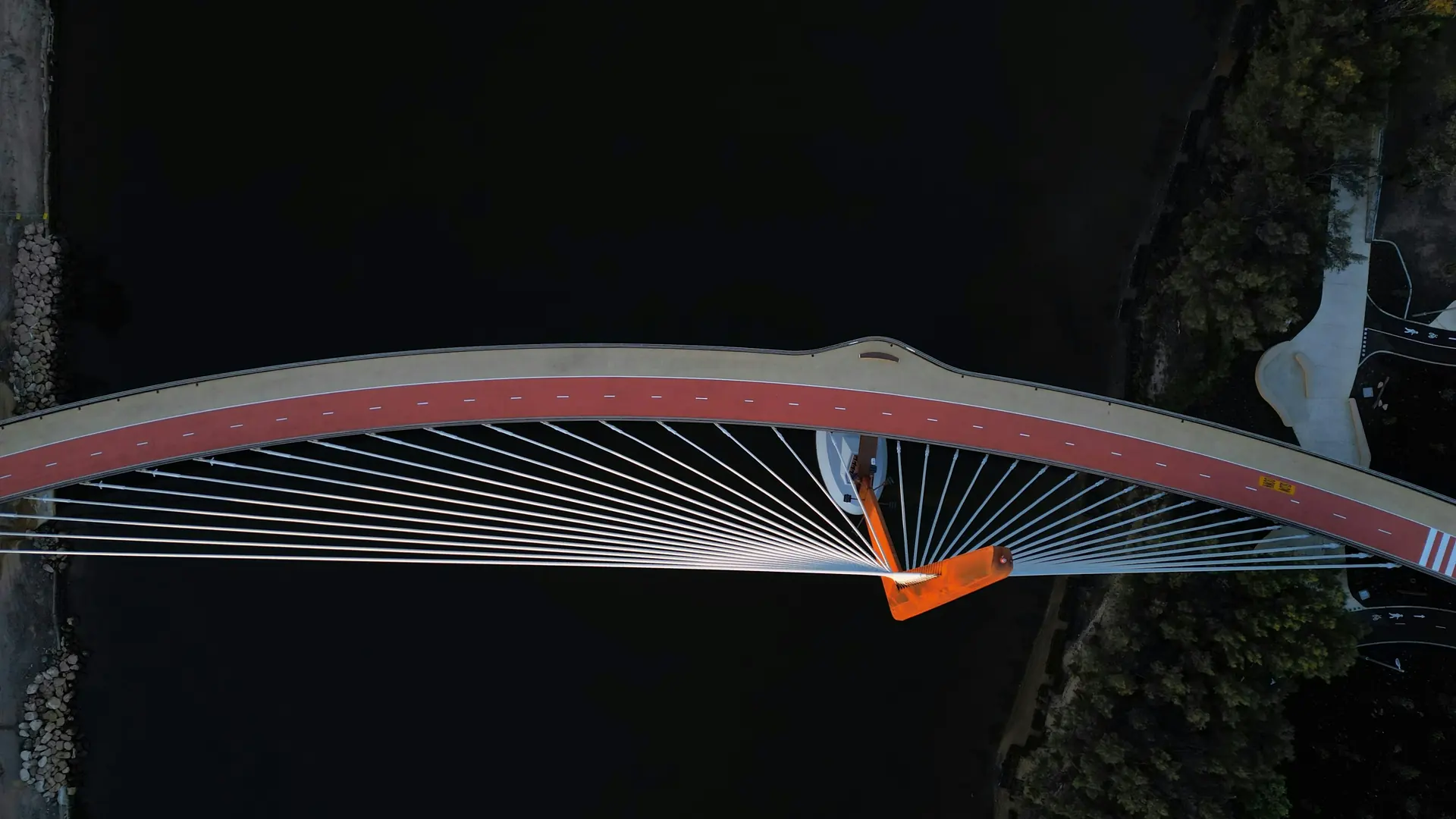 A cable-stayed bridge arching across dark water at night, seen from above