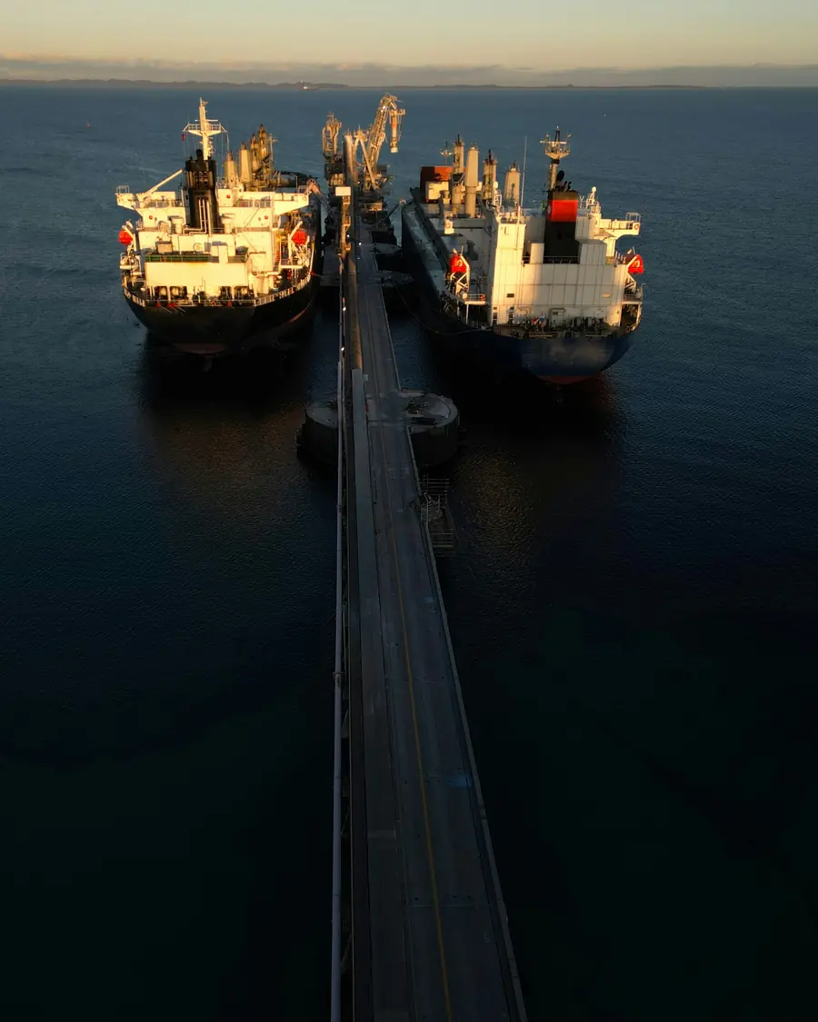 Two vessels berthed either side of a long jetty at dusk