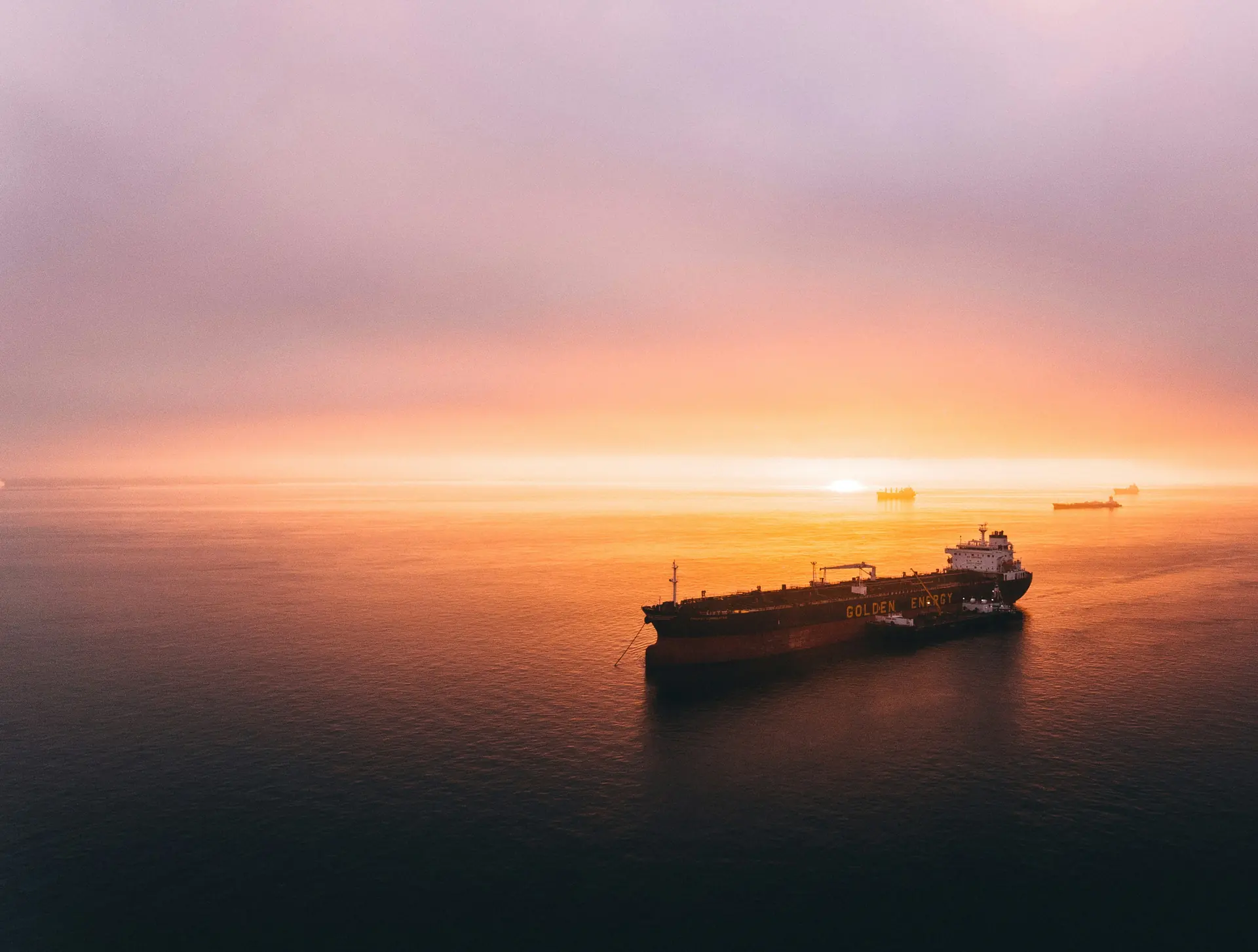 An oil tanker at anchor on calm open water at dusk, with further vessels on the horizon